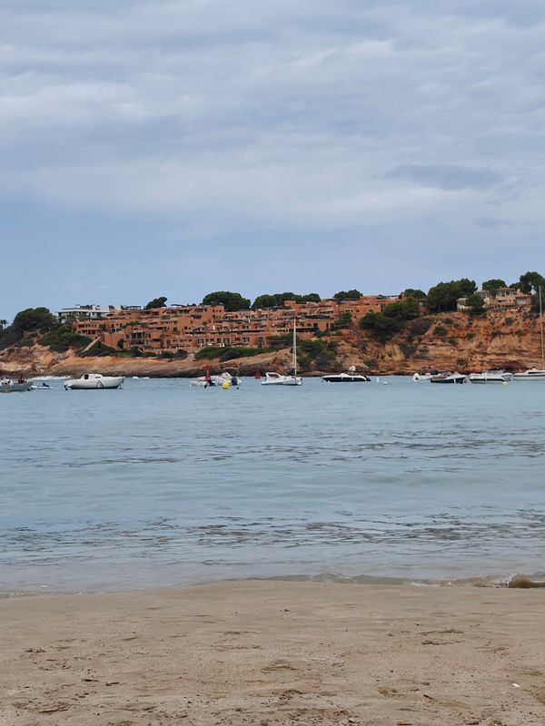 A serene beach scene with wet sand and shallow reflective water under a cloudy sky after a storm.