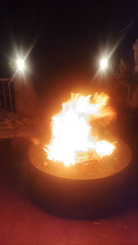 A vibrant fire burns in a fire pit at night, surrounded by glowing lanterns.