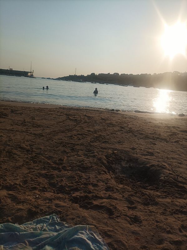 A serene beach scene at sunset with people swimming in the water.