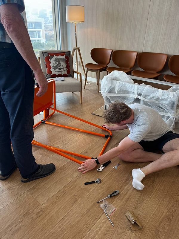 Two individuals are assembling a large orange carriage in a modern living space.