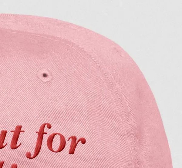 A close-up view of a pink hat featuring embroidered text.