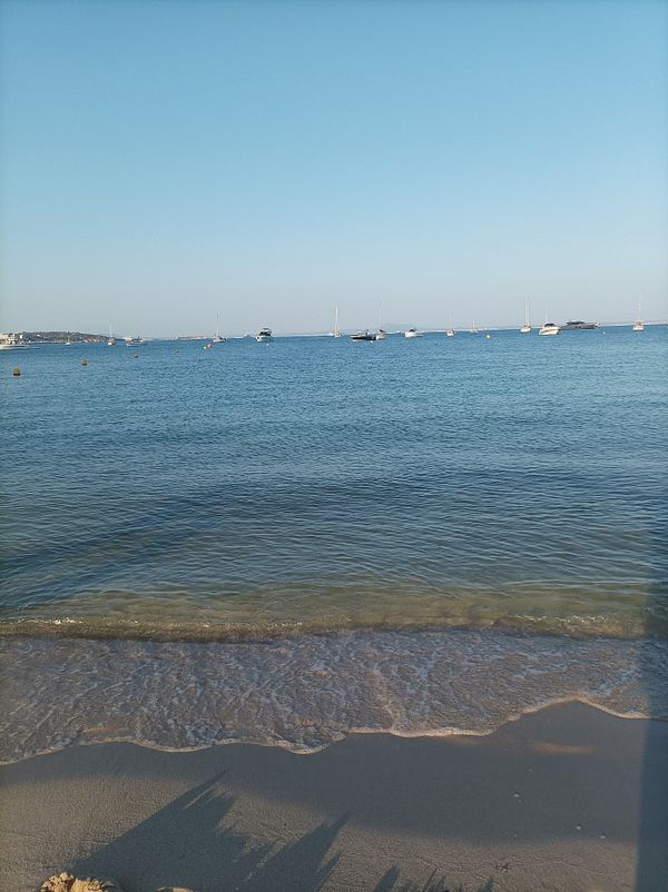A serene beach scene with calm waters and distant boats under a clear blue sky.