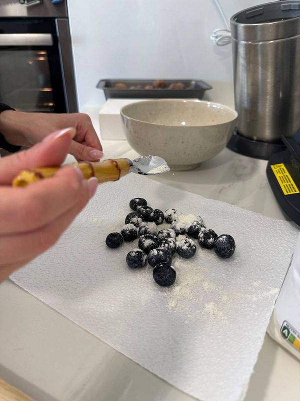 A person is preparing blueberries for a butter cake by coating them in flour.