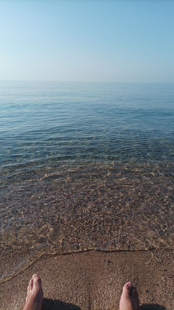 A serene view of calm waters at Sant Pol de Mar, Cataluña, with feet in the foreground.