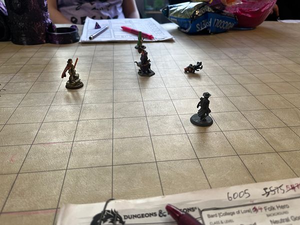 Group of four diverse young adults playing a tabletop role-playing game with character sheets, dice, and a laptop on a table.