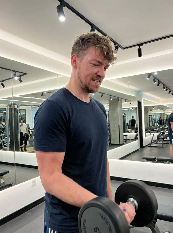 A man is lifting a dumbbell in a modern gym setting.