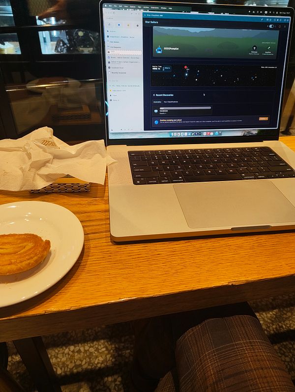 A workspace setup in a cafe featuring a laptop, a pastry, and a casual atmosphere.