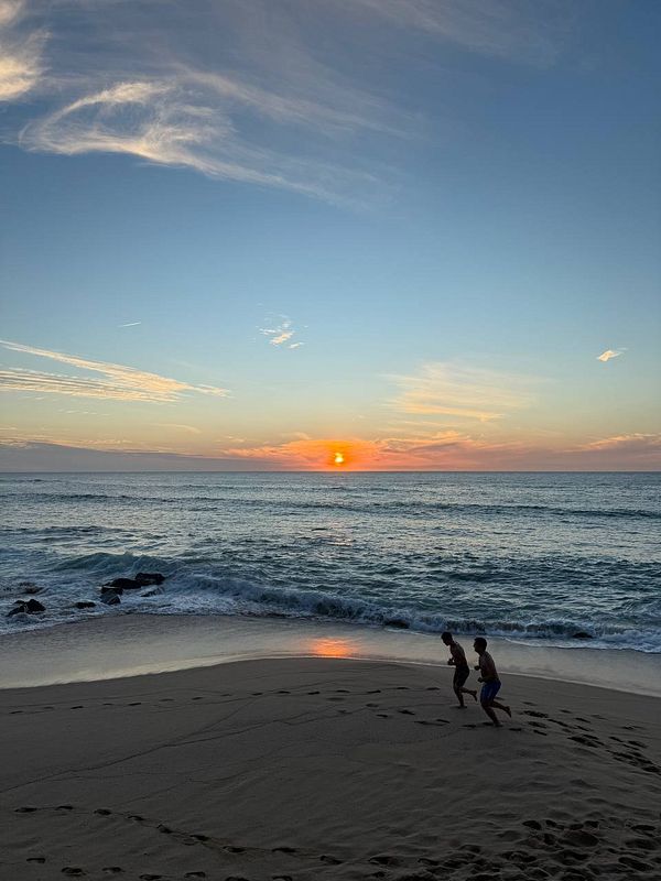 A serene beach scene at sunset with two individuals running along the shore.