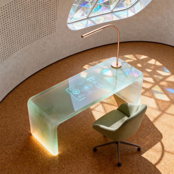 A minimalist home office features a curved, translucent desk with softly glowing iridescent edges and an embedded holographic interface on its surface. A slender rose-gold arc lamp sits on the desk beside a sage green upholstered swivel chair on casters. The space has warm cork flooring, a white curved wall with perforated acoustic detailing, and a faceted prismatic window that casts colorful geometric light across the floor and desk.