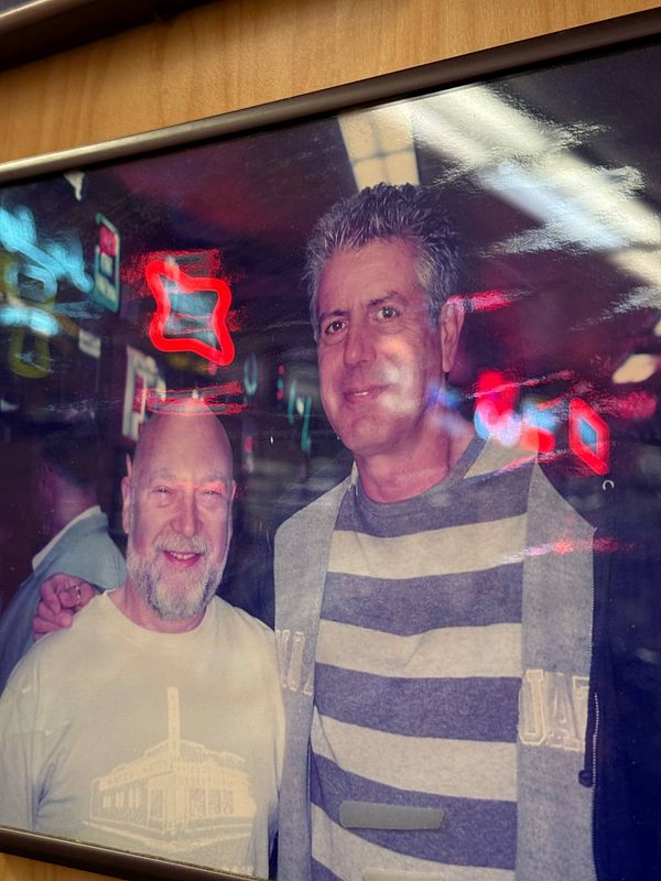 A nighttime street view of Katz's Delicatessen illuminated by neon signs and bustling with people and traffic.