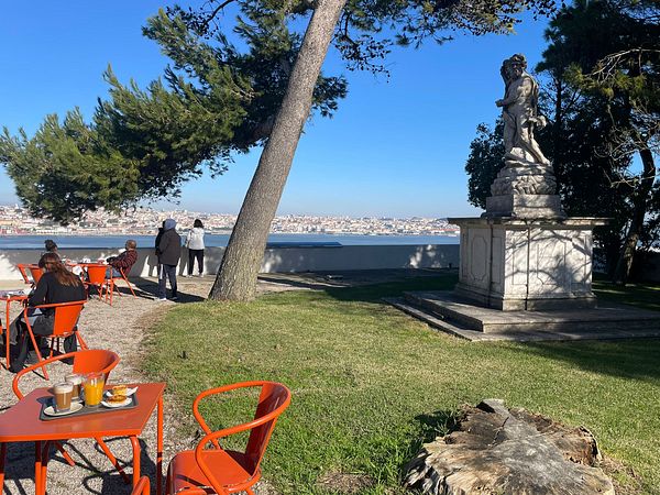 A scenic view of a park in Portugal featuring a statue, outdoor seating, and a distant cityscape.