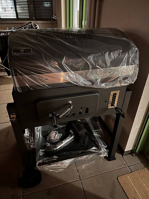 A new barbecue grill is displayed, still wrapped in protective plastic.