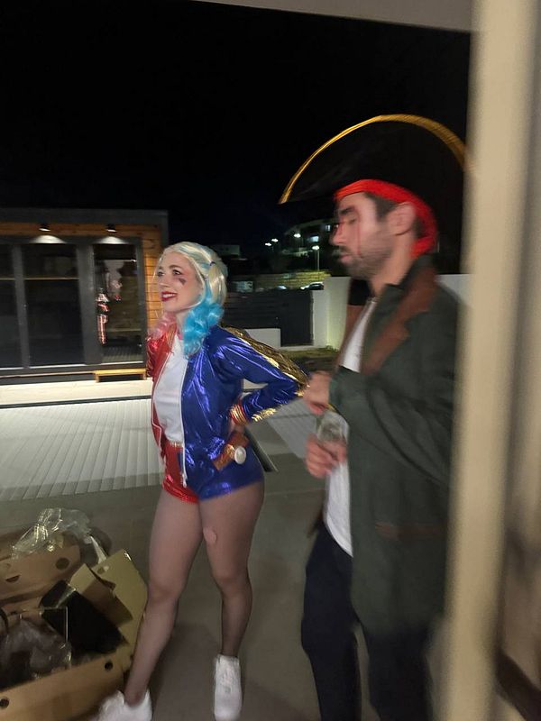 A woman in a colorful costume poses playfully while a man in a pirate outfit stands beside her.