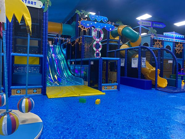 Indoor children's play area featuring slides, tunnels, climbing structures, and beach-themed decorations.