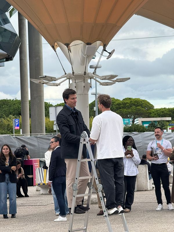 Toto Wolff is engaged in conversation with another individual while standing on a ladder in a public space.