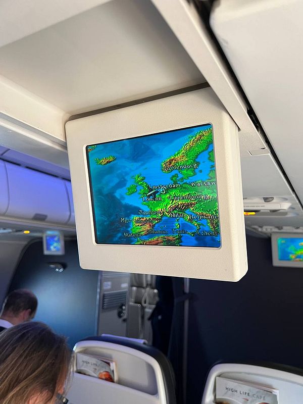 An in-flight screen displays a map of Europe with flight information.