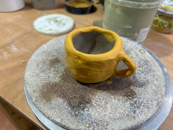 A ceramics workshop setup showing several pottery items, materials, and tools arranged on a wooden table.