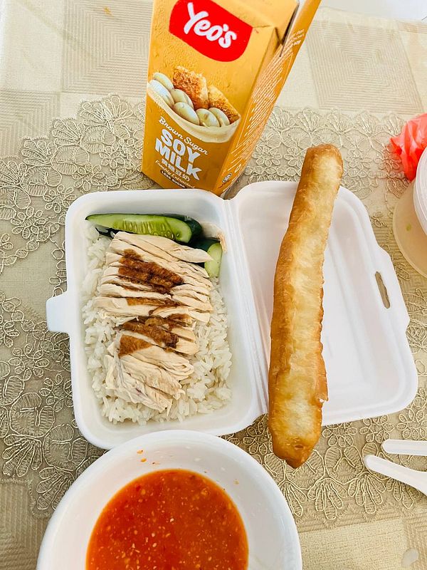 A meal featuring chicken rice, a side of cucumber, a dipping sauce, and a drink.