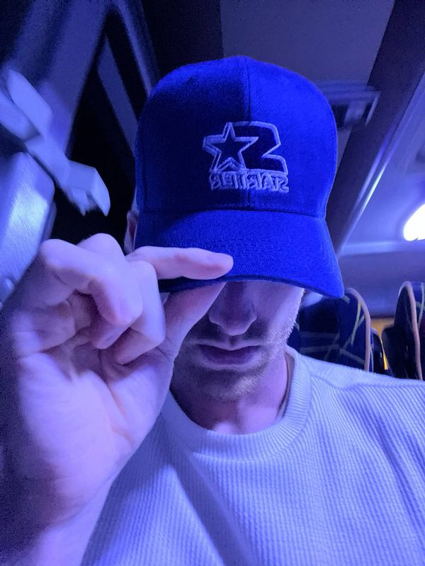 A person wearing a blue cap is sitting on a bus, partially obscuring their face.