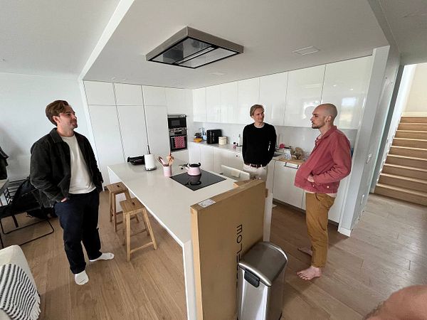 Three individuals are engaged in conversation in a modern kitchen space.