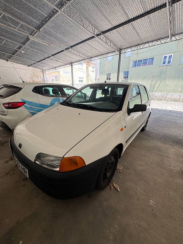 A white car is parked in a covered area alongside another vehicle.
