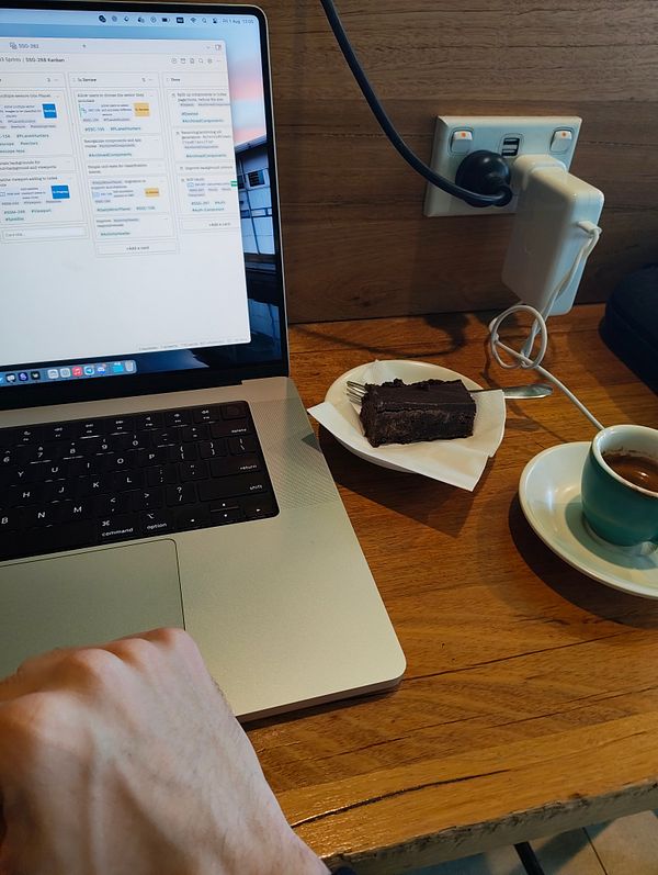 A workspace setup at a café featuring a laptop, dessert, and coffee.