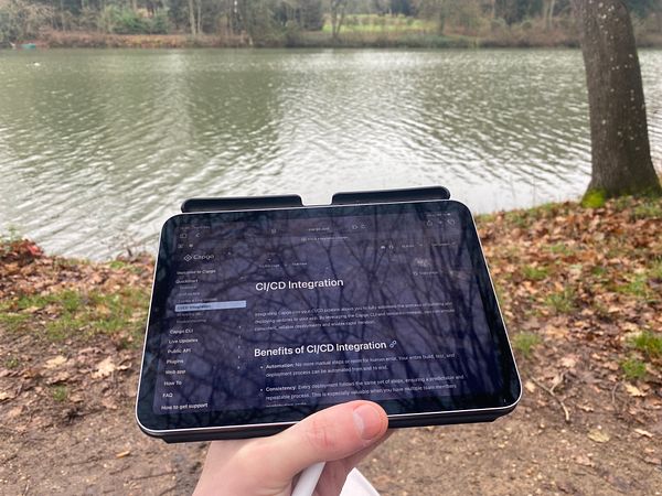 A person is sitting by a lake, holding a tablet displaying information about CI/CD integration.