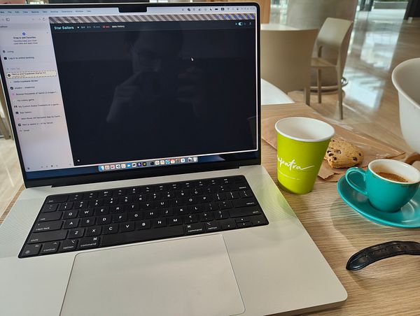 A laptop displaying a dark mode interface sits on a table alongside a coffee cup and a cookie.