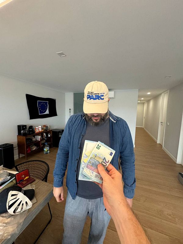 A person is handing over cash to another individual wearing a cap in a coworking space.