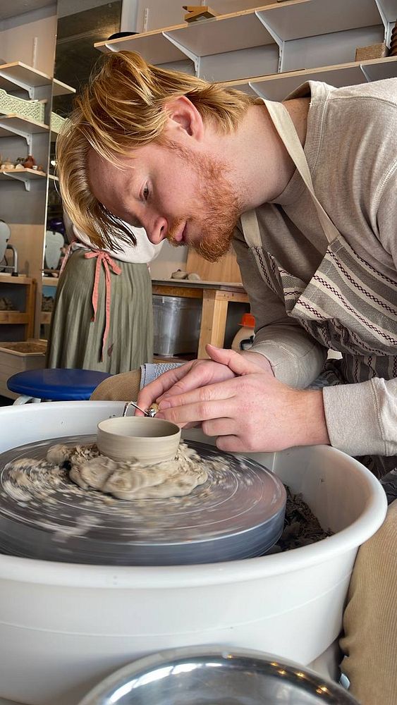 A young couple engaged in pottery making together, shaping clay on a pottery wheel.