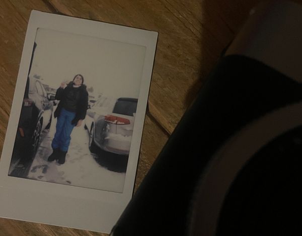 A photograph of a snowboarder in mid-air during a jump in a snowy, forested mountain area.