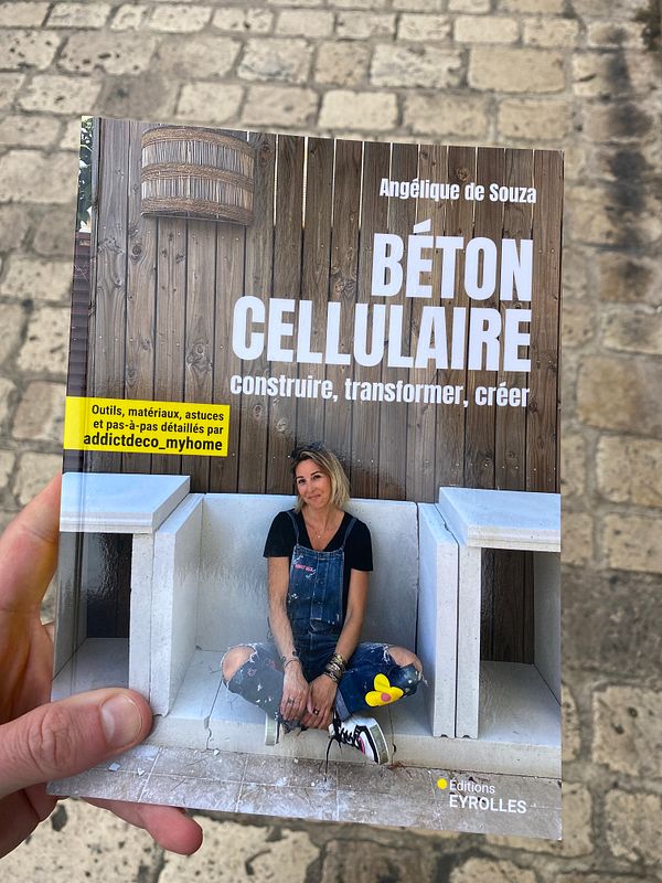 Cover of the book 'Béton Cellulaire' by Angélique de Souza, showing the author sitting on a white concrete bench against a wooden background.