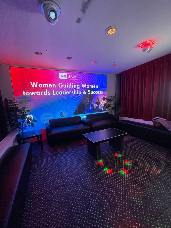 The image depicts a cozy event space in Taipei with a focus on women's leadership.