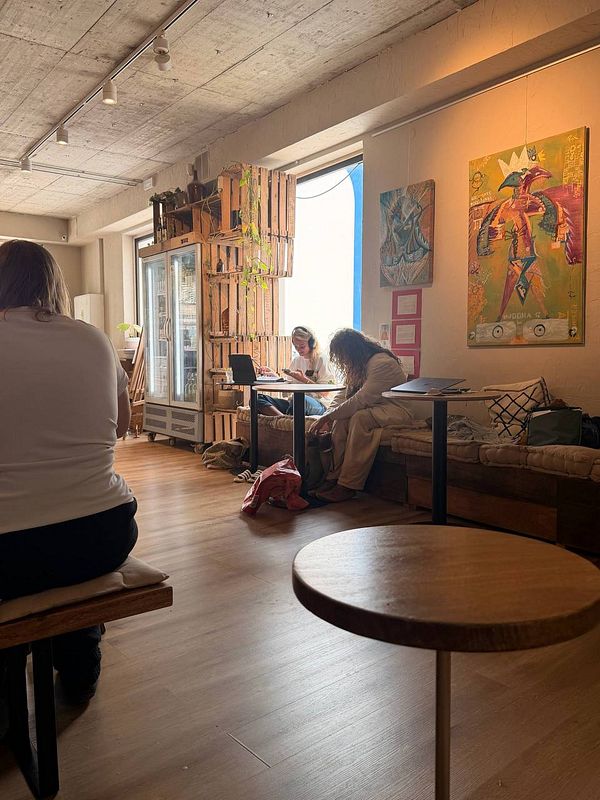 A woman in a yellow top smiling next to a man in a patterned shirt is surrounded by a café interior setting.