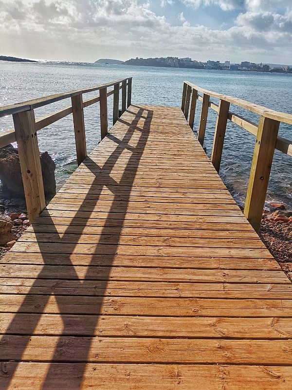 A wooden pier extends over calm waters, leading towards a scenic view of the coastline.