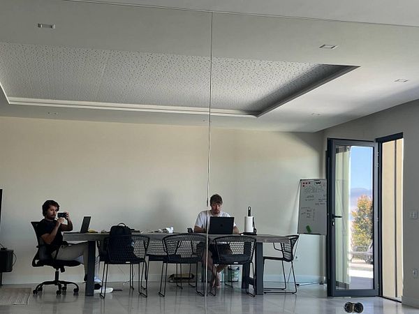 Two individuals are working in a modern coworking space with a large mirror reflecting their activities.