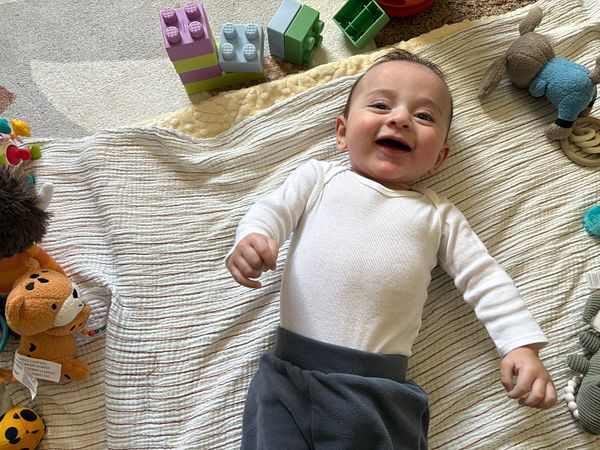 A joyful baby lies on a soft blanket surrounded by colorful toys.