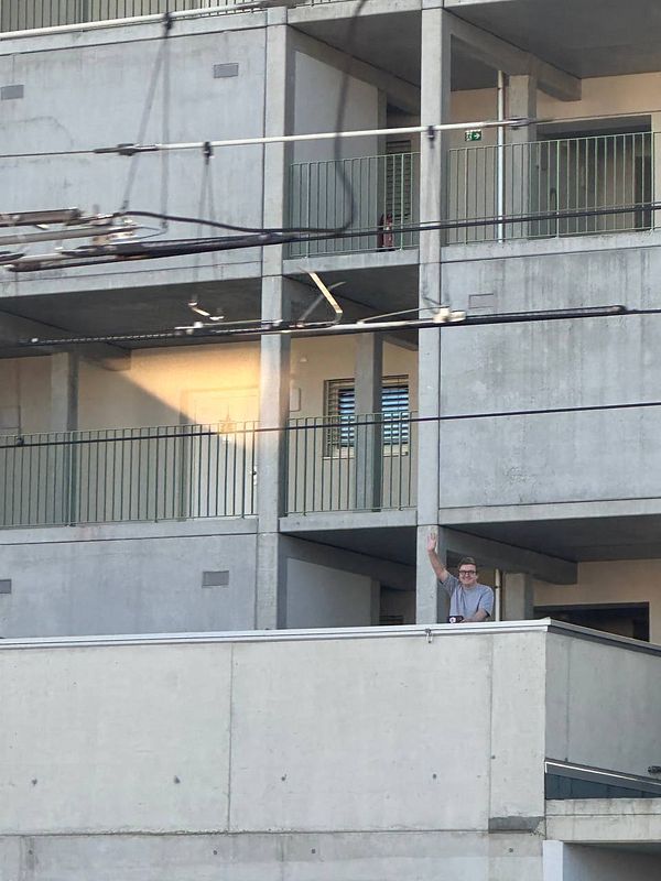 A man waves from a balcony as a train approaches.