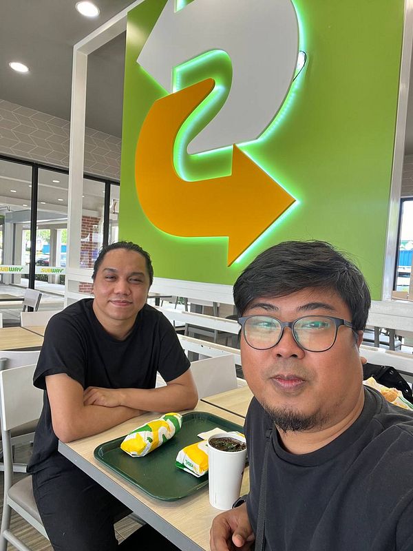 Two individuals are seated at a table in a Subway restaurant, enjoying food and drinks.