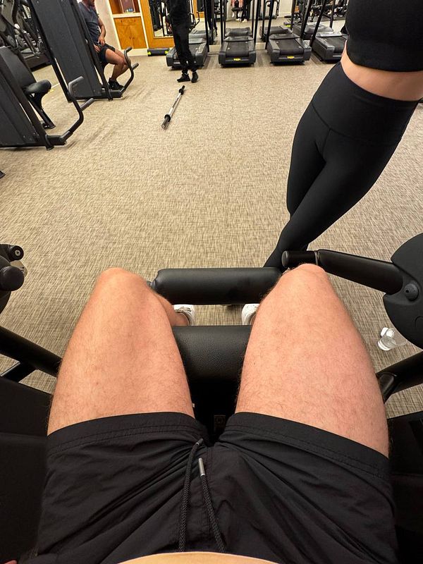 A gym scene featuring a person using a leg exercise machine.