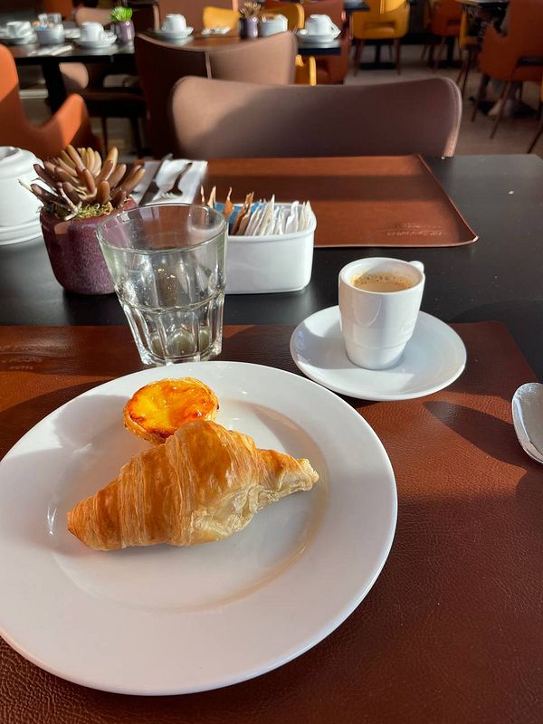 A delightful hotel breakfast featuring a croissant, a custard tart, and a cup of espresso.