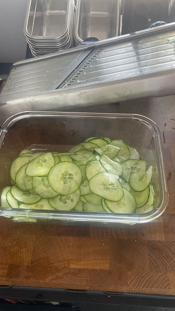 A container filled with freshly sliced cucumbers on a wooden countertop.