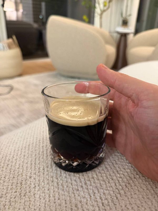 A hand holds a glass of Guinness beer on a textured surface.