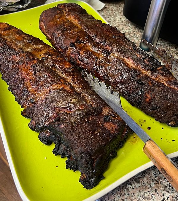 Two large smoked ribs are displayed on a bright green platter.