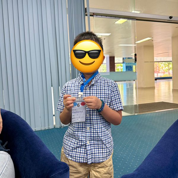 A young boy proudly holds a school identification badge in a bright, modern environment.