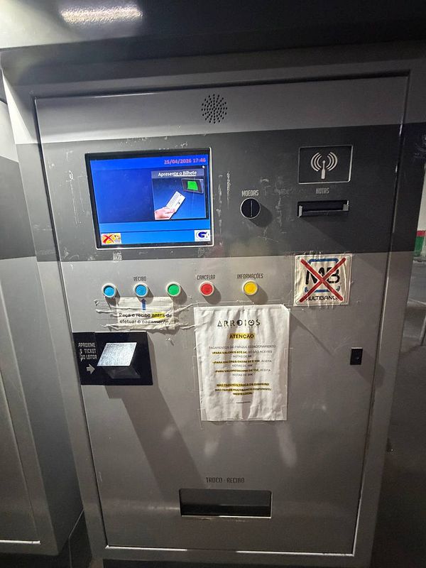 Photo of a parking payment machine in Portugal with a paper notice explaining payment details and a small change box below it.