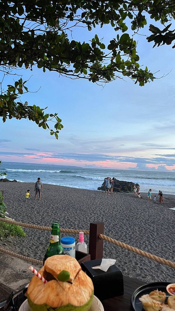 A scenic beach view at sunset with people enjoying the shoreline and a table set for dinner.
