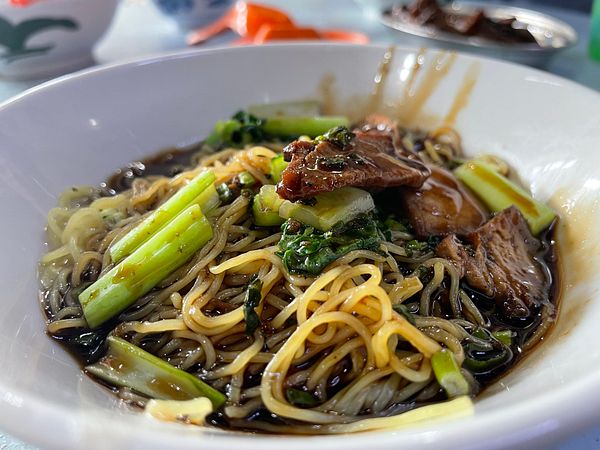 A bowl of wan tan mee featuring noodles, greens, and meat.