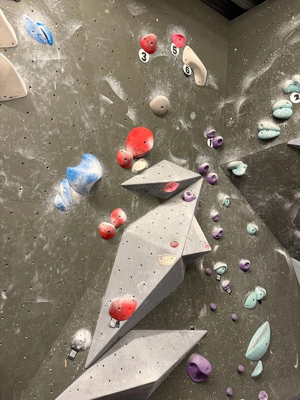 A close-up photo of a person's hands showing signs of wear and calluses from bouldering, gripping a gym climbing hold.