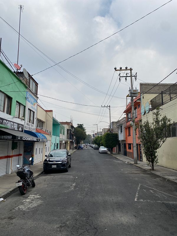 A quiet street in Mexico City lined with colorful buildings and parked cars.